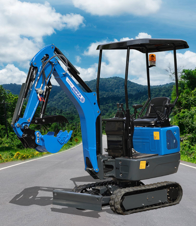 Sininen minikaivinkone seisoo asfalttitiellä, taustalla vuoristomaisema ja sininen taivas pilvillä. Kaivinkoneessa on musta katos ja oranssi varoitusvalo.